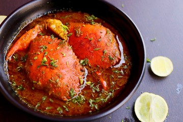 Indian Cuisine, Spicy Crabs Curry in red gravy, garnished with fresh coriander and lemon wedges or lemon slices on dark moody background