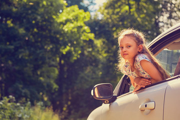 Fun happy enjoying traveling kid girl looking from the car window with open mouth on summer bright...