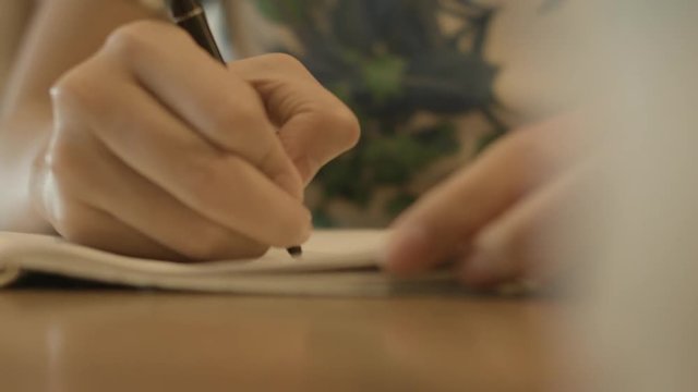 Close Up Of Hand Holding A Pen And Writing On A Notebook
