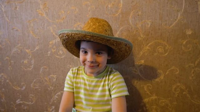 The boy in the straw hat. Changing the image. The camera revolves around the object. Against the wall with Wallpaper. Rustic image. 4K video