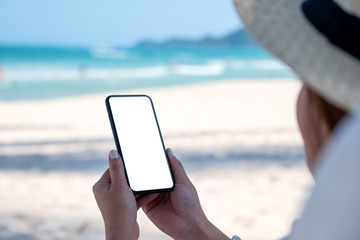 A woman holding white mobile phone with blank desktop screen with blue sky background on the beach