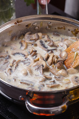 young woman in a gray apron adds milk to mushroom sauce
