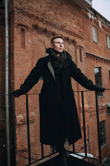 Portrait of a young man in a coat with a fur collar. On the background of a brick wall.