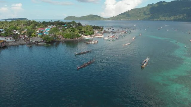 Aerial: kora-kora traditional canoe annual race in Bandaneira and speed boats sailing in the beautiful sea of the Banda Islands, Maluku, Indonesia. Native cinelike D-log color profile