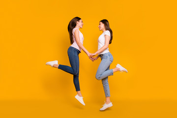 Fototapeta na wymiar Full length body size profile side view portrait of nice charming winsome sweet attractive cheerful slim fit thin straight-haired girls holding hands isolated on bright vivid shine yellow background