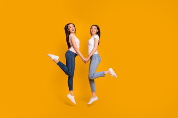 Fototapeta na wymiar Full length body size profile side view portrait of nice charming sweet attractive cheerful slim fit straight-haired girls holding hands having fun isolated on bright vivid shine yellow background