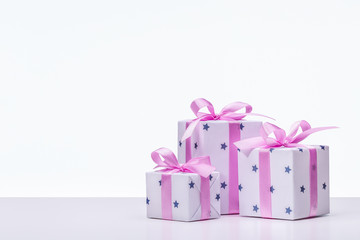 Stylish boxes with gifts in white paper in stars, decorated with pink satin ribbon with bows. Copy space.