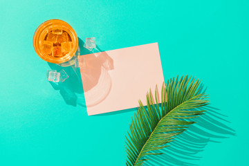 Tropical cocktail with ice cubes, palm leaf  and pink paper card note on vivid blue background....
