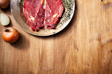 Top view of two fresh raw meat seasoned with salt ,pepper and rosemary on vintage plate next to chopped white onion.