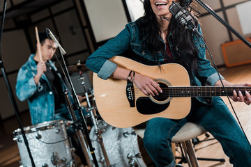 partial view of musician playing guitar and singing while mixed race man playing drums in recording studio