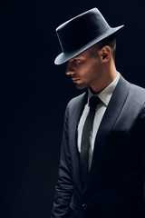 Fototapeta na wymiar Profile view portrait oh handsome man in black suit and hat on dark background