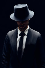 Handsome confident man in black suit and hat on dark background