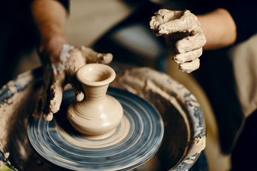 Man potter working on potters wheel making ceramic pot from clay in pottery workshop