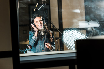 Naklejka premium beautiful, inspired musician singing near microphone in recording studio