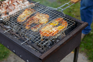 Shashlik (or shashlik) and salmon steaks preparing on a barbecue grill over charcoal. Grilled cubes of pork meat on metal skewer. Outdoor.