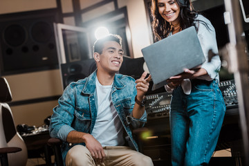 smiling multicultural sound producers using laptop in recording studio
