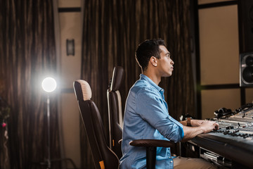 Fototapeta na wymiar concentrated sound producer sitting in office chair and working at mixing console