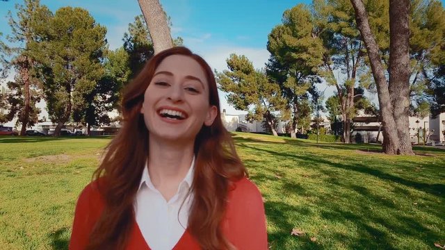 A happy, attractive, young, caucasian woman at the park, turns her head to the camera, and lets out a really big laugh. Slow motion - Steadicam - Close up.