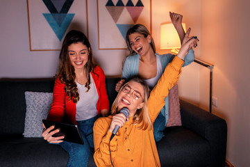 Three female friends having fun playing karaoke at home.