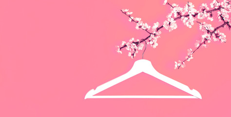 Creative fashion beauty concept. White wooden hanger hanging on the spring flowering branch on pink background. Spring sale concept discount store shopping empty hanger. Flat lay top view copy space.