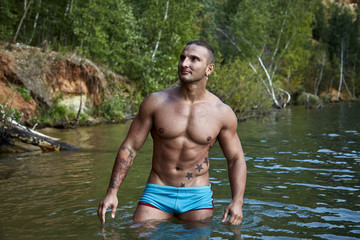 Wet cute guy with a perfect muscular torso stands in the water and stares sidewards