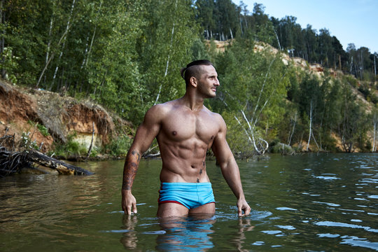 Muscle god with perfect strong body looks squinting into the distance of the lake