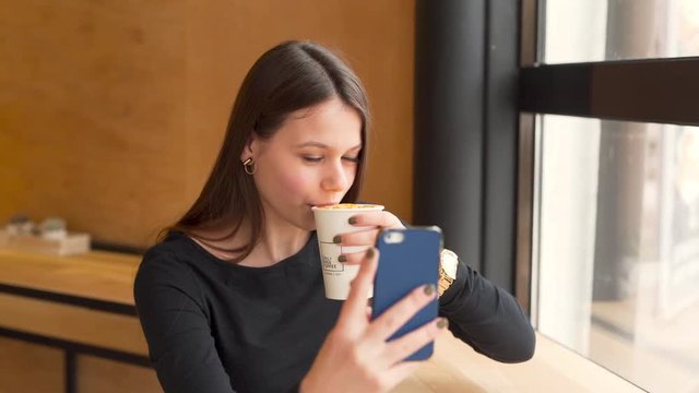 Young Woman Moves Smartphone Around While Taking A Selfie And Takes Sip From Cup In Coffee Shop