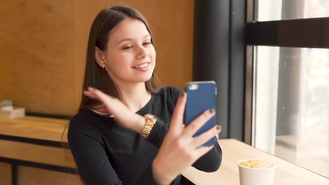 Young Woman Moves Smartphone Around While Taking A Selfie And Puts Cup On Table In Coffee Shop