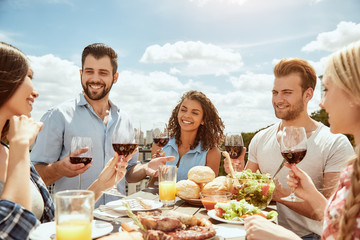 First summer barbecue! Group of happy young people are eating fresh food, talking and drinking wine...