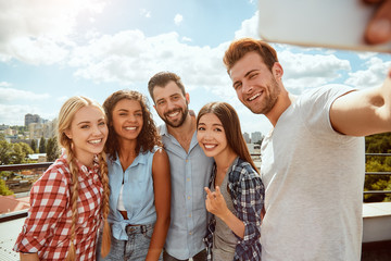 Collecting happy moments. Group of cheerful and young people are making selfie and smiling at camera while standing on the roof