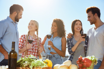 Having great time with friends. Group of young and happy people smiling and drinking wine while standing on the roof with friends.