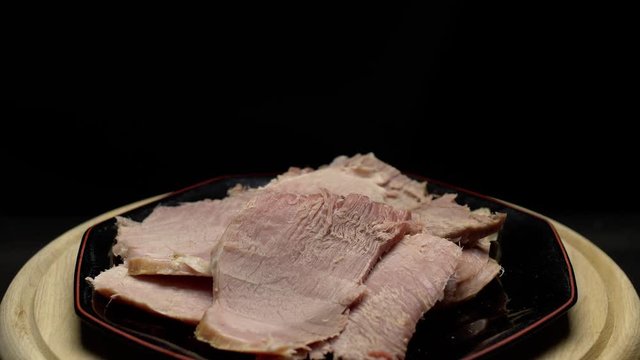 Easter cooked ham sliced on a plate; rotating on a turntable; isolated on a black background.