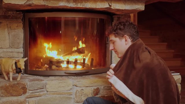 Man Wraps Himself in a Blanket to Keep Warm by the Fire.
