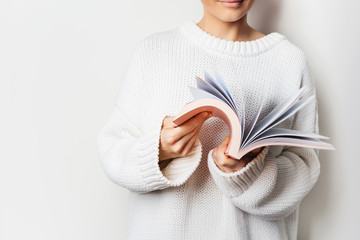 Close view of woman in white woolen sweater holding an open book with pink cover in hands. Mock up...