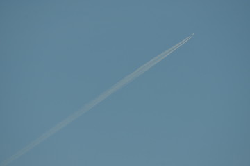 commercial aircraft at very high altitude with white contrail on cloudless blue sky
