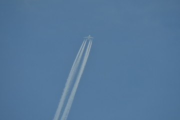 commercial aircraft at very high altitude with white contrail on cloudless blue sky