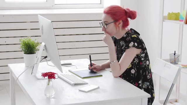 Concept of freelancing or office work. Young female photographer, retoucher or graphic designer with colored hair works at a computer and smokes vape