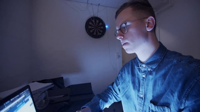 Serious young nerdy guy is sitting late at night in his room trolling people on internet.
