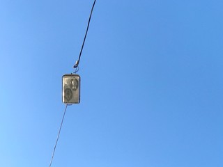 Outdoor vintage street light hanging with electric cable above a street against deep clear blue sky background. 