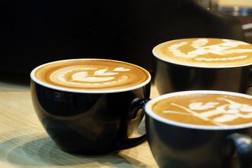 Close up a beautiful latte art on top of a hot latte coffee in a black cup,wooden dinning table background 