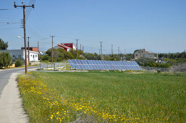 Fototapeta na wymiar Solar electricity panels on green field near houses in Cyprus. Renewable alternative energy