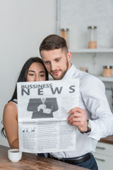 Fototapeta na wymiar brunette girl and handsome man in suit reading business newspaper in kitchen