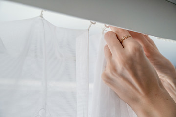 Woman hangs up or removes white curtains indoors, close-up