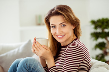 Fototapeta premium Close up side profile photo beautiful amazing she her lady calm kindhearted hold hot warm beverage hands arms wear striped pullover clothes sit comfort cozy divan flat house living room indoors