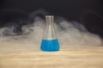 flask with blue liquid in smoke over black background. chemical analysis