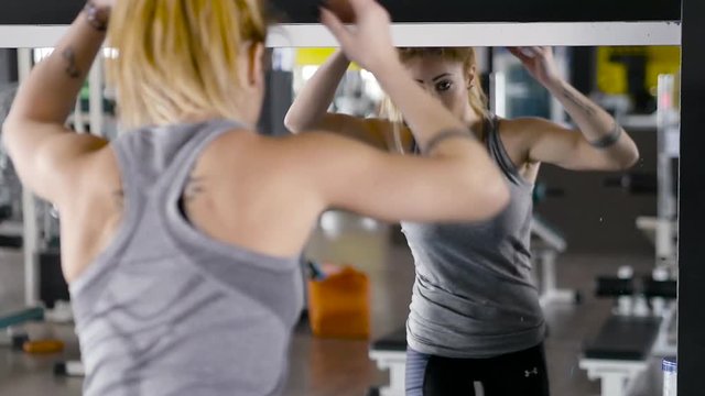 Close-up of a pretty blonde woman fixing her hair and clothing in the mirror at the gym