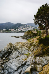 Coastal landscape with rocks and stones next to the beach, the sea and a coastal village with clear blue sky.