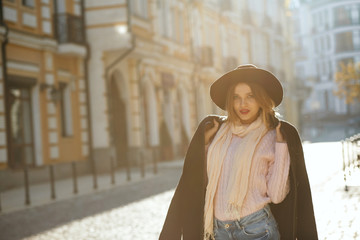 Street fashion concept: elegant young girl wearing hat and sweater posing with sun light. Empty space