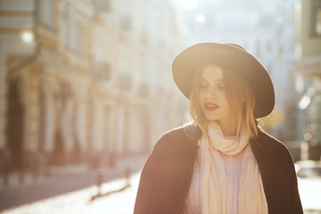 Closeup portrait of lovely blonde girl wearing hat and coat posing with sun light. Empty space