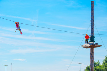 Little brave caucasian girl using a zip line. An indefinited man lend a helping hand.